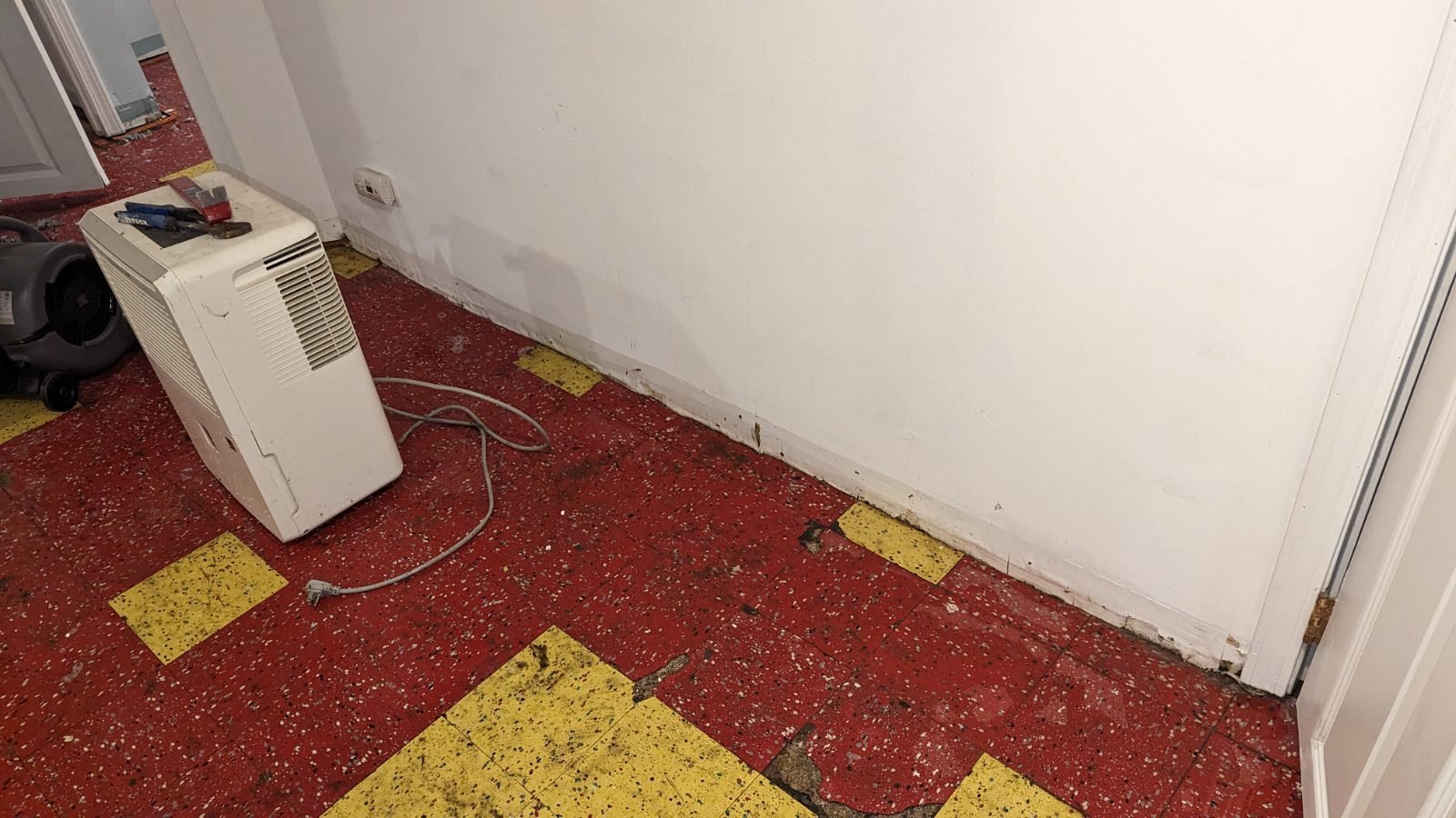 Dehumidifier and air mover beside an exposed wall base